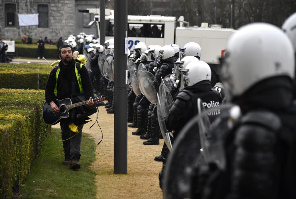 A man plays a guitar as he walks by a line of police during a demonstration against COVID-19 measures in Brussels, Sunday, Jan. 23, 2022. Demonstrators gathered in the Belgian capital to protest what they regard as overly extreme measures by the government to fight the COVID-19 pandemic, including a vaccine pass regulating access to certain places and activities and possible compulsory vaccines. (AP Photo/Geert Vanden Wijngaert)