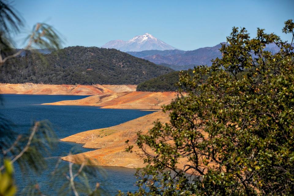 Receding waters in a lake leave a bare, brown shoreline.