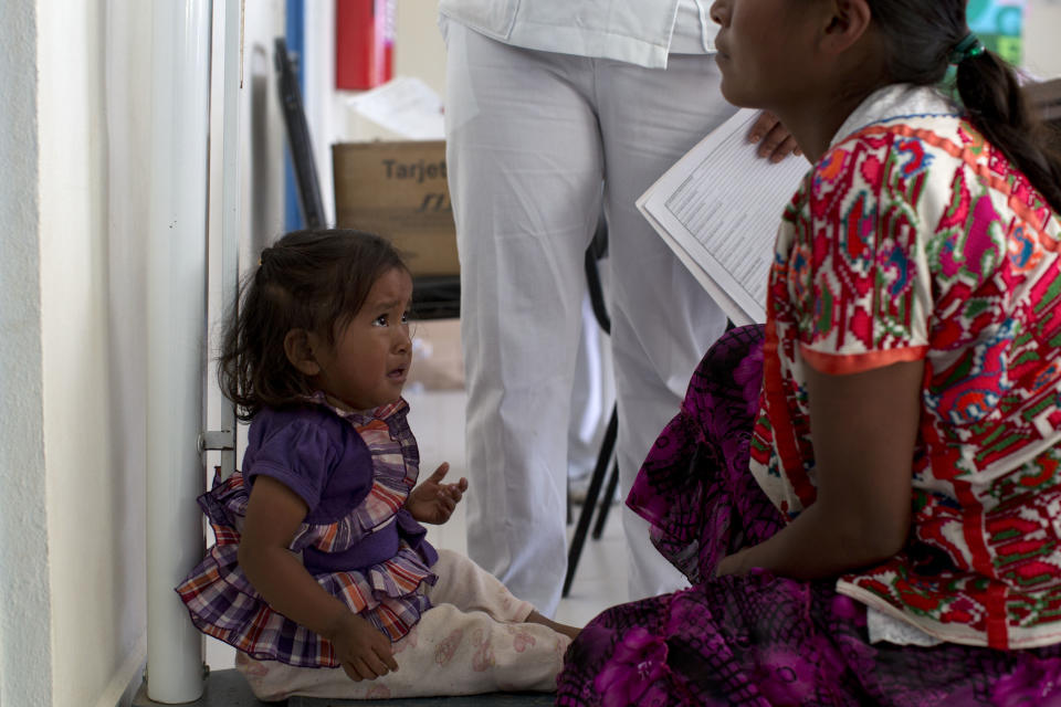 In this Tuesday, Feb. 11, 2014 photo, a Mixteco indigenous girl looks up at her mother as she gets weighed at a health clinic in Cochoapa El Grande, Mexico. The head of Mexico’s anti-poverty program drew criticism Monday, May 5, 2014, after she warned Indian mothers that government aid programs would only help support their first three children. (AP Photo/Dario Lopez-Mills)