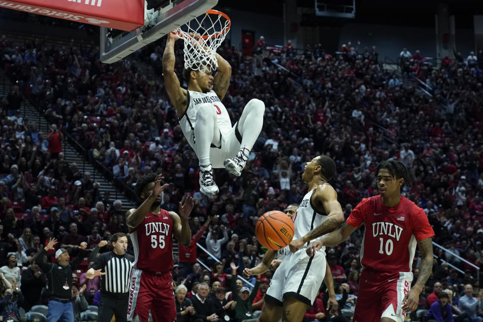San Diego State guard Matt Bradley hangs on the rim after a dunk during the first half of an NCAA college basketball game against UNLV Saturday, Feb. 11, 2023, in San Diego. (AP Photo/Gregory Bull)