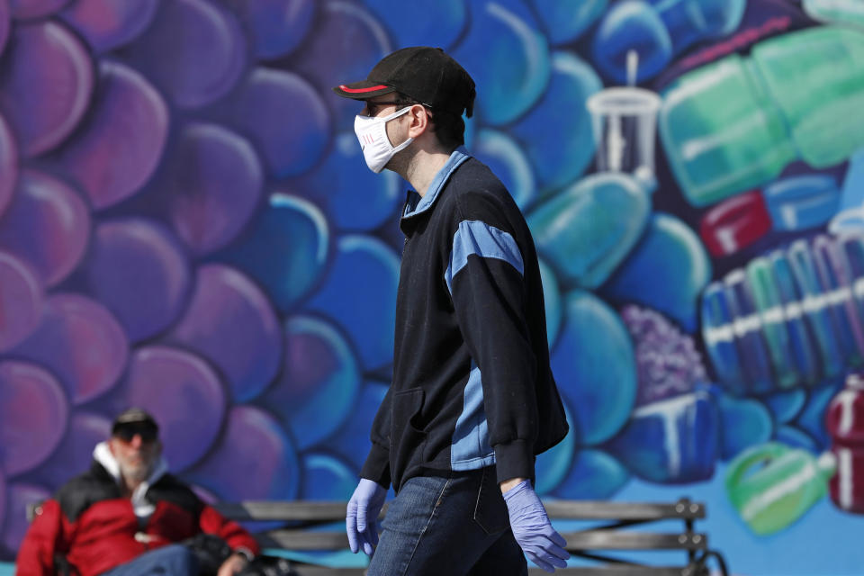 A pedestrian wears a face mask as he walks past a mural of a fish while strolling on the boardwalk at Coney Island, Thursday, April 2, 2020, in the Brooklyn borough of New York amid concerns about spreading or contracting the coronavirus. The Trump administration is formalizing new guidance to recommend that many, if not all, Americans wear face coverings when leaving home, in an effort to slow the spread of COVID-19. The recommendations were still being finalized Thursday, and would apply at least to those who live in areas hard-hit by community transmission of the virus. (AP Photo/Kathy Willens)