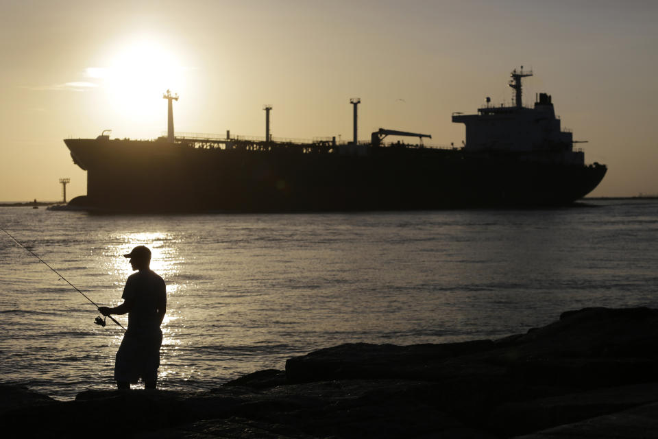 FILE - In this July 21, 2015, file photo, an oil tanker passes a fisherman as it enters a channel near Port Aransas, Texas, heading for the Port of Corpus Christi. The U.S., seemingly awash in crude oil after an energy boom sent thousands of workers scurrying to the plains of Texas and North Dakota, will begin exporting oil for the first time since the 1973 oil embargo.  (AP Photo/Eric Gay, File)