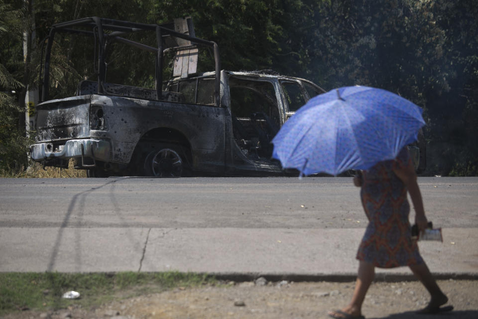 A pedestrian walks past a charred truck that belongs to Michoacan state police, after it was burned during an attack in El Aguaje, Mexico, Monday, Oct. 14, 2019. At least 13 police officers were killed and three others injured Monday in the ambush. (AP Photo/Armando Solis)