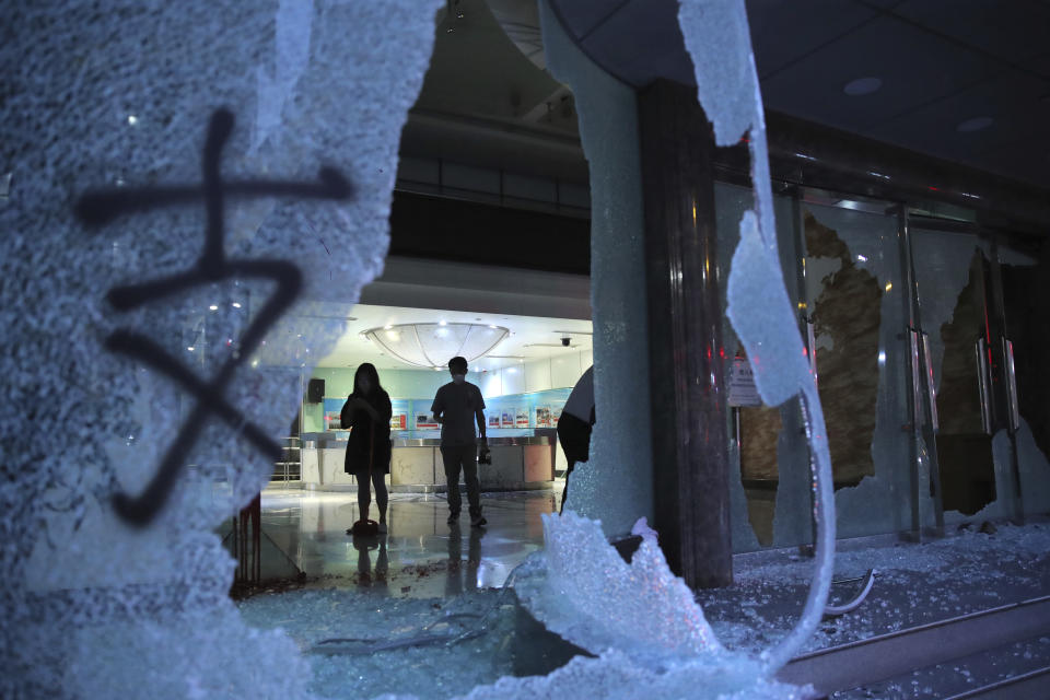 People stand in the lobby of the offices of China's Xinhua News Agency damaged by protesters in Hong Kong, Saturday, Nov. 2, 2019. Hong Kong riot police fired multiple rounds of tear gas and used a water cannon Saturday to break up a rally by thousands of masked protesters demanding meaningful autonomy after Beijing indicated it could tighten its grip on the Chinese territory. (AP Photo/Kin Cheung)