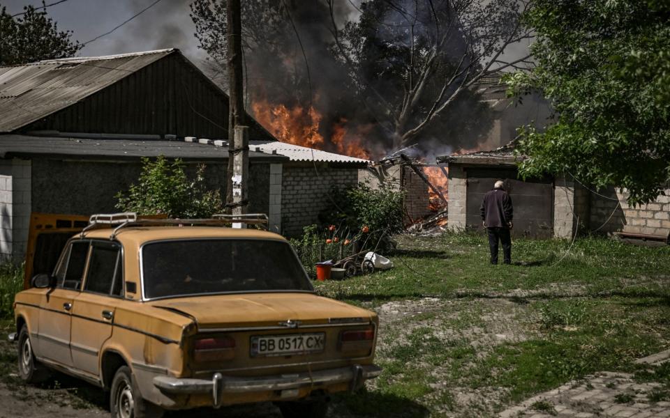 An elderly man stands in front of a burning house garage after shelling in the city of Lysytsansk  - ARIS MESSINIS /AFP