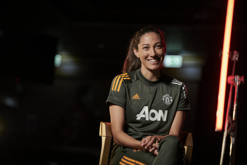Christen Press in a black Manchester United kit sits on a chair.