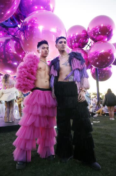 Two people pose for a fashion portrait in front of a sculpture of pink globes