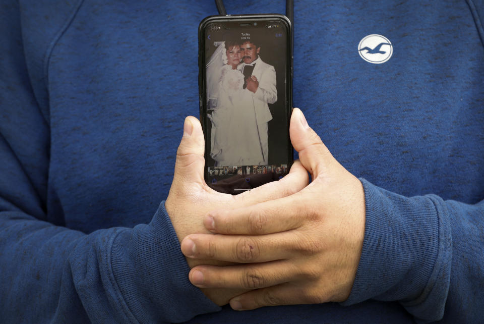 Omar Martinez holds his cell phone displaying a photo from his parents' wedding, Saturday, April 25, 2020, in West Liberty, Iowa. Martinez's family had been living the American dream after immigrating from Mexico in the 1990s and settling in this small town in eastern Iowa, but their lives fell apart after coronavirus infections spread from his mother to his sister and his father. Now he is planning his father's funeral while hoping his sister recovers in a hospital intensive care unit. He is grateful his mother is better and appreciates the community's support. (AP Photo/Charlie Neibergall)