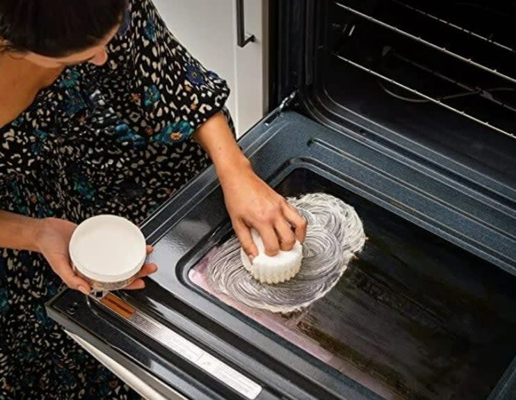 Person cleaning an open oven door with the Scrub Daddy sponge and Scrub Daddy cleaning paste