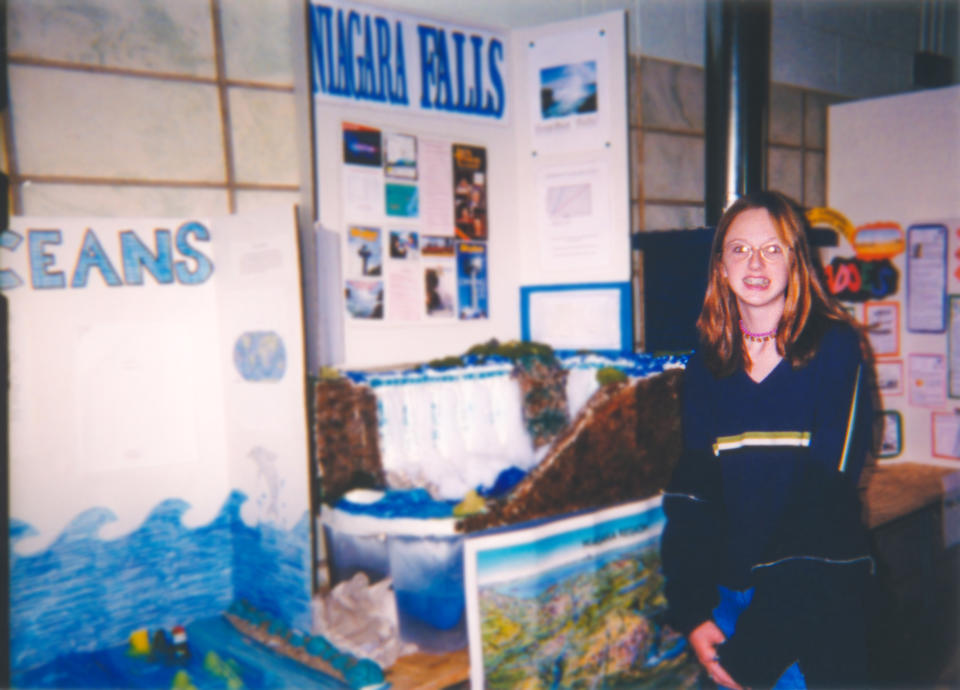 Woman kneeling by a school project titled "Water Falls," with displays and diagrams behind her