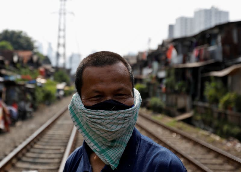 A man covers his face with a napkin along rail tracks in Jakarta