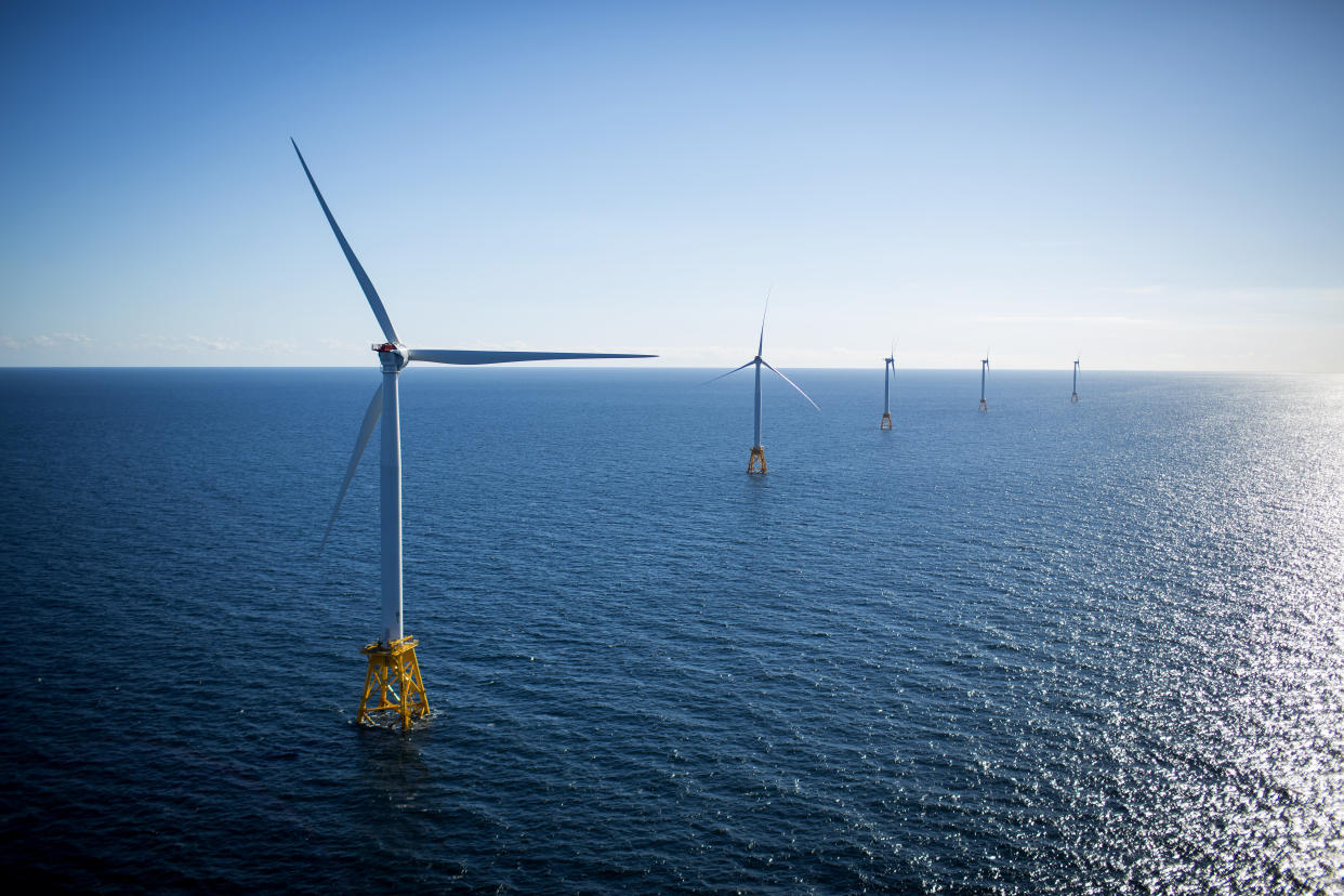 Five large wind turbines rest on yellow platforms in the ocean.