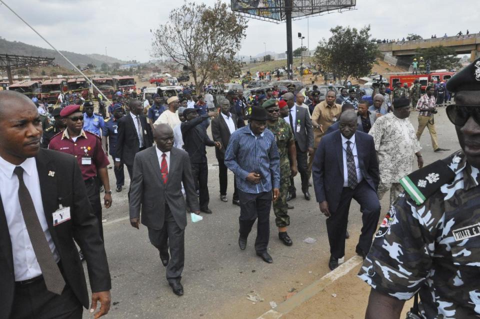 Nigeria President, Goodluck Jonathan, centre, visits the site of an explosion at a bus park in Abuja, Nigeria, Monday, April. 14, 2014. An explosion blasted through a busy commuter bus station on the outskirts of Nigeria's capital, Abuja, before 7 a.m. (0600 GMT) Monday as hundreds of people were traveling to work. Many are feared dead. Reporters saw rescue workers and police gathering body parts. The blast ripped a hole 4 feet deep (1.2 meters) in the ground of Nyanya Motor Park about 16 kilometers (10 miles) from the city center and destroyed more than 30 vehicles, causing secondary explosions as their fuel tanks ignited and burned. (AP Photo/ Gbemiga Olamikan)