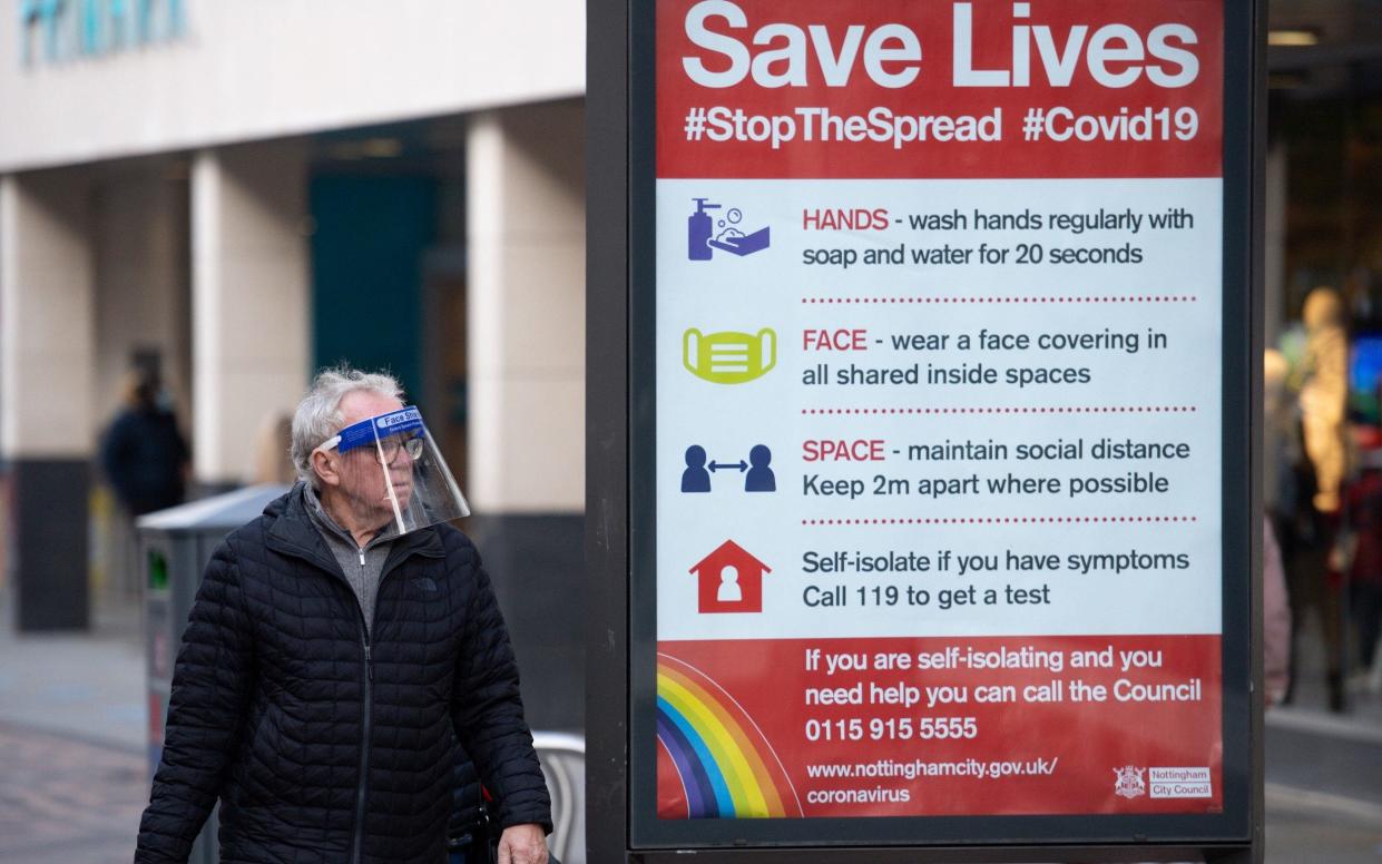 A pedestrian wearing a face shield walks past a sign in Nottingham advising how to stop the spread of coronavirus - Jacob King/PA