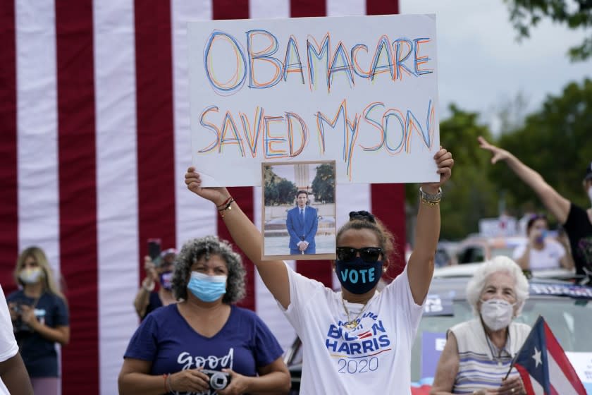 Adelys Ferro holds a sign in support of Obamacare as former President Barack Obama speaks while campaigning for Democratic presidential candidate former Vice President Joe Biden at Florida International University, Saturday, Oct. 24, 2020, in North Miami, Fla. (AP Photo/Lynne Sladky)