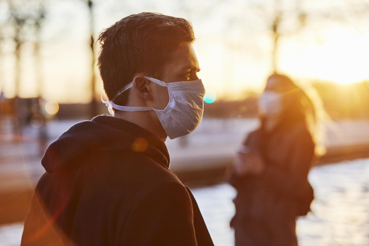 Young man and young woman in urban environment using protective face masks