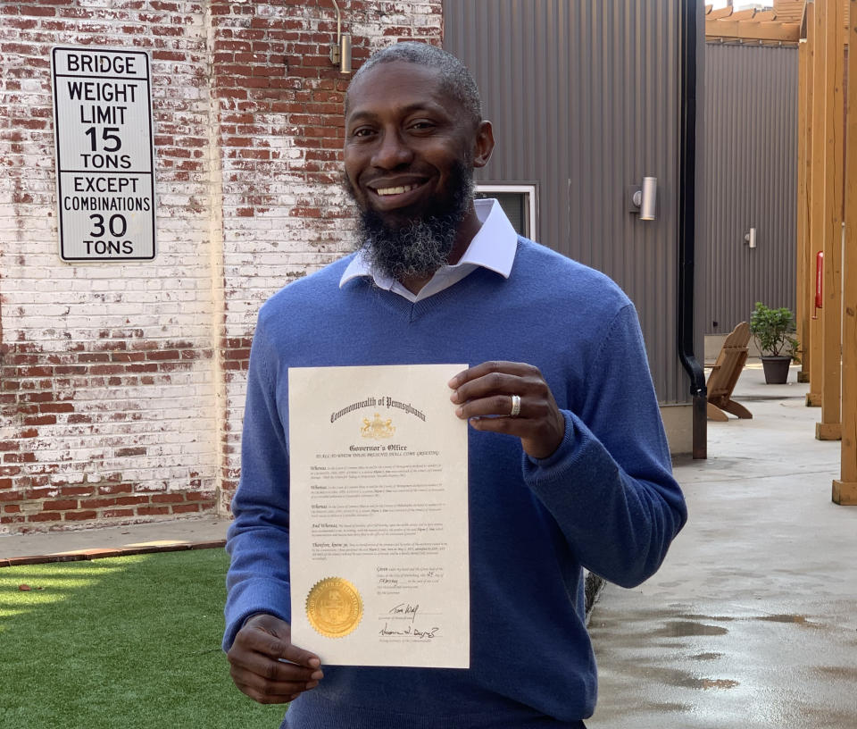 Akeem Sims, in crisp blue shirt and blue sweater, shows his certification for pardon, with its gold stamp.