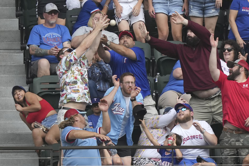 Fans in the stands try to catch the homer hit by Texas Rangers' Corey Seager during the second inning of a baseball game against the Colorado Rockies in Arlington, Texas, Sunday, May 21, 2023. (AP Photo/LM Otero)