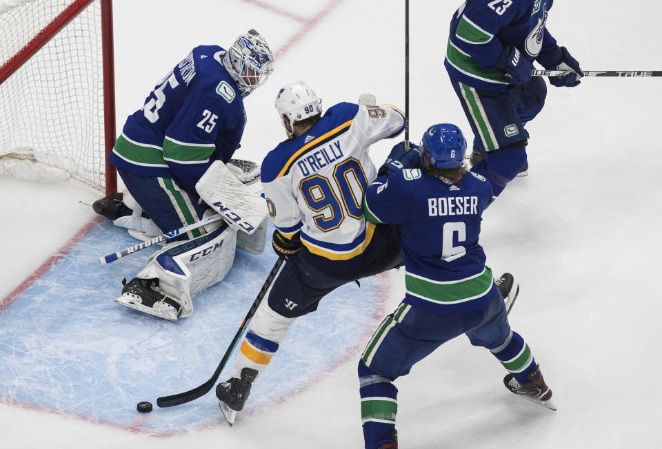 Vancouver Canucks goalie Jacob Markstrom (25) makes a save on St. Louis Blues' Ryan O'Reilly (90) as Brock Boeser (6) defends during overtime in Game 3 of an NHL hockey first-round playoff series, Sunday, Aug. 16, 2020, in Edmonton, Alberta. (Jason Franson/The Canadian Press via AP)