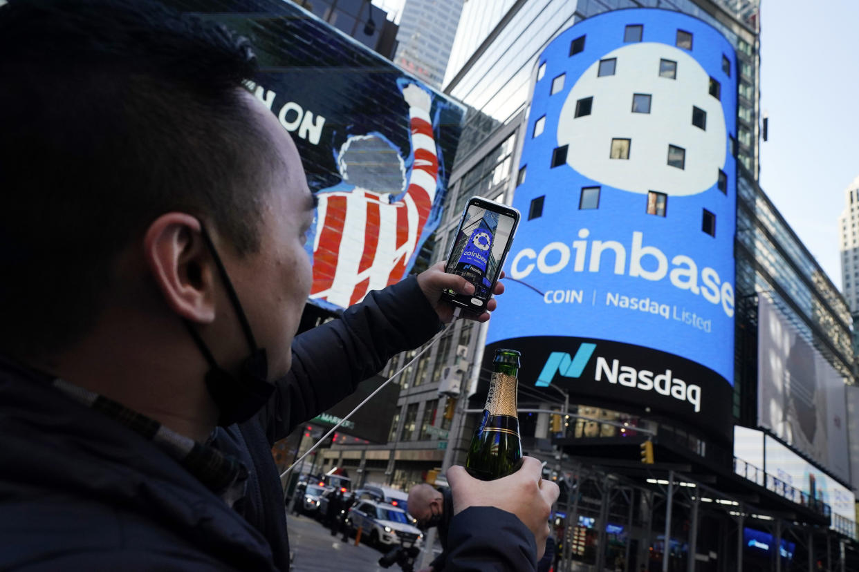 Coinbase employee Daniel Huynh holds a celebratory bottle of champagne as he photographs outside the Nasdaq MarketSite, in New York's Times Square, Wednesday, April 14, 2021. Wall Street will be focused on Coinbase Wednesday with the digital currency exchange becoming a publicly traded company. (AP Photo/Richard Drew)