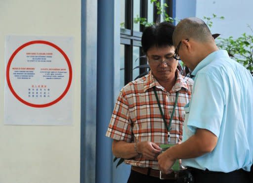 A presiding officer (L) checks a voter polling card at a polling centre in Singapore. Singapore's ruling People's Action Party (PAP) was returned to power on Sunday with a huge majority but lost a key district to the opposition, costing a senior cabinet minister his job