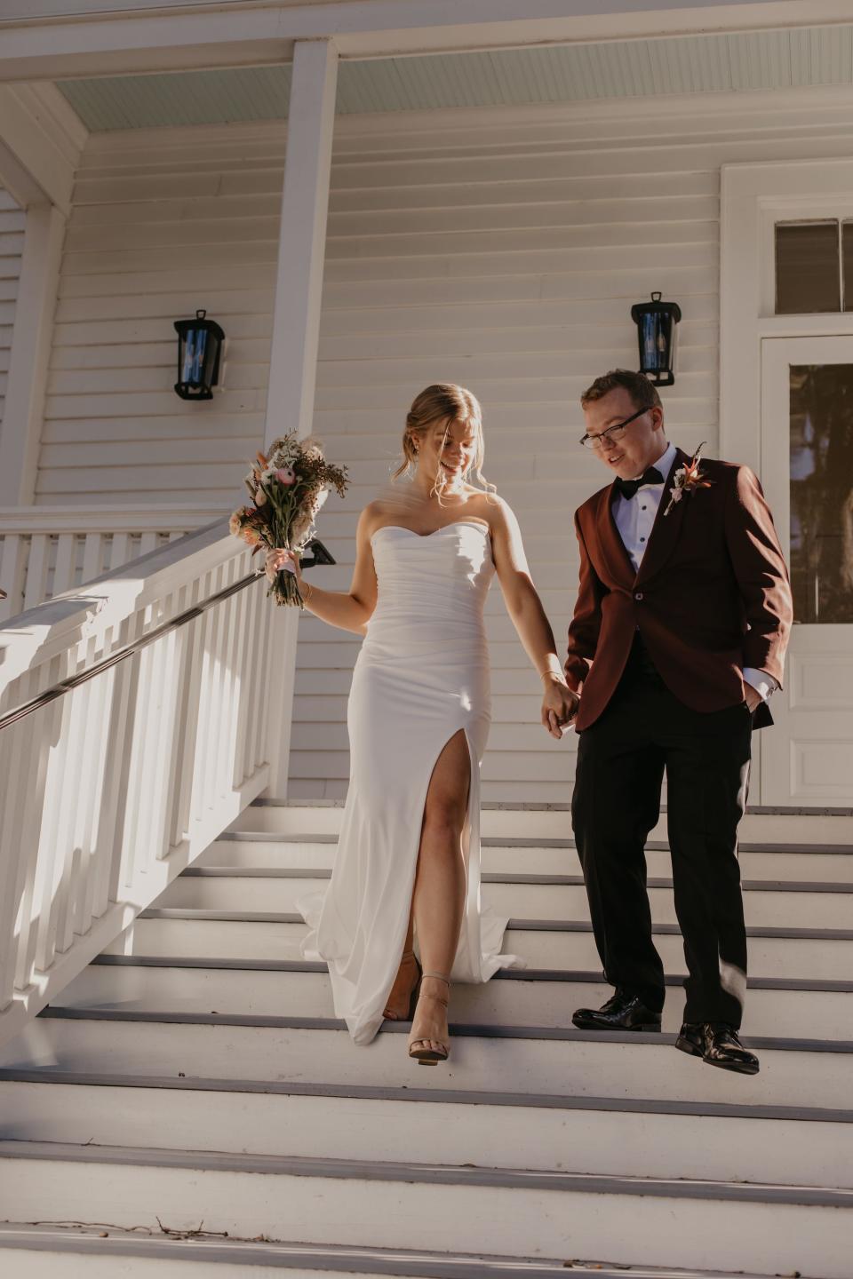 A bride and groom hold hands and walk down a staircase together.