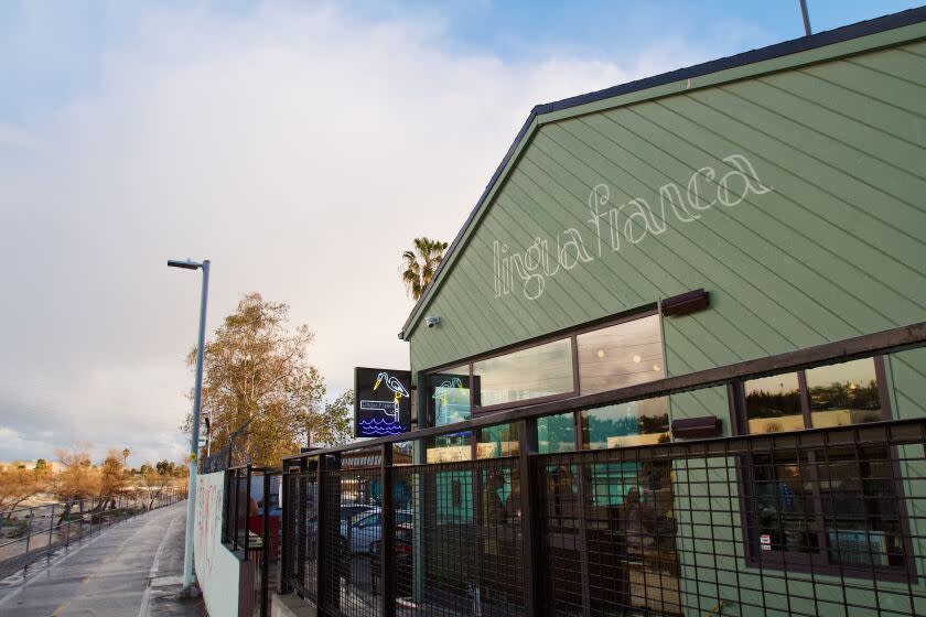 A photo of the restaurant's exterior: Muted green with wooden angled planks; to the left is a bike path and the L.A. River