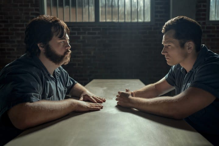 Paul Walter Hauser and Taron Egerton sit at a small table in prison, facing each other, in a scene from Black Bird.