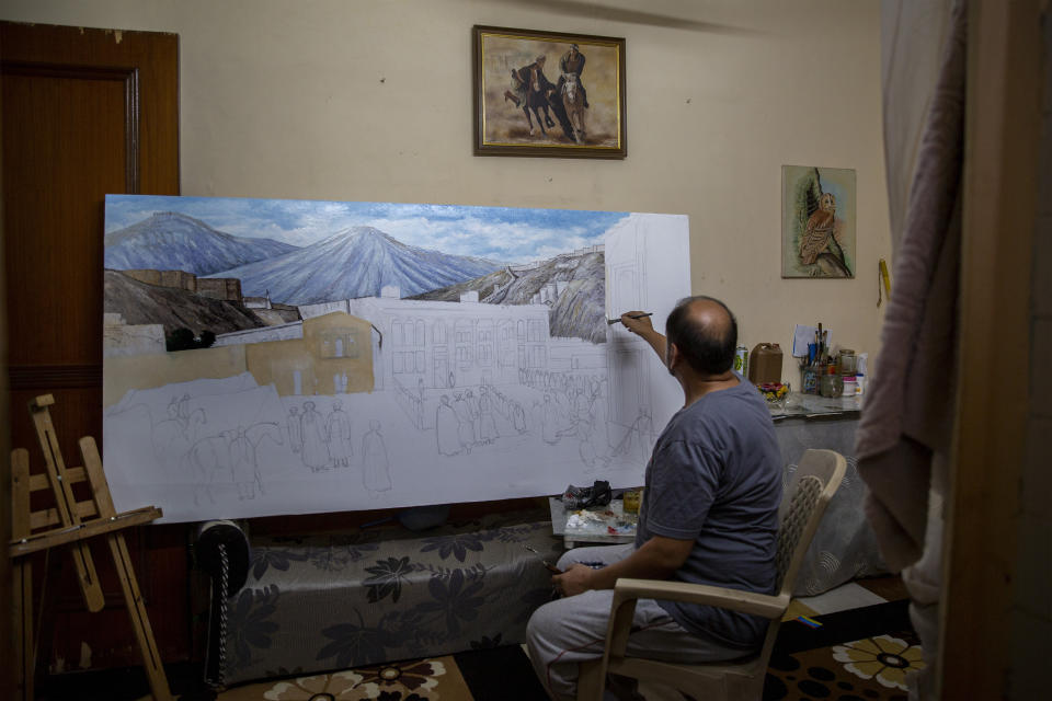 Akbar Farhad, an Afghan artist, paints an old Kabul market and the ruins of "Bala-e- Hissar," or the High Fort, an ancient citadel that housed Afghan rulers for centuries, inside a rented accommodation in New Delhi, India on Aug. 13, 2021. Farhad has been living in New Delhi since 2018. He left Kabul after facing threats from insurgents demanding he close his studio. Like thousands of other Afghan refugees in India, their plans to someday return home were dashed by the Taliban's shockingly swift takeover of the country. (AP Photo/Altaf Qadri)
