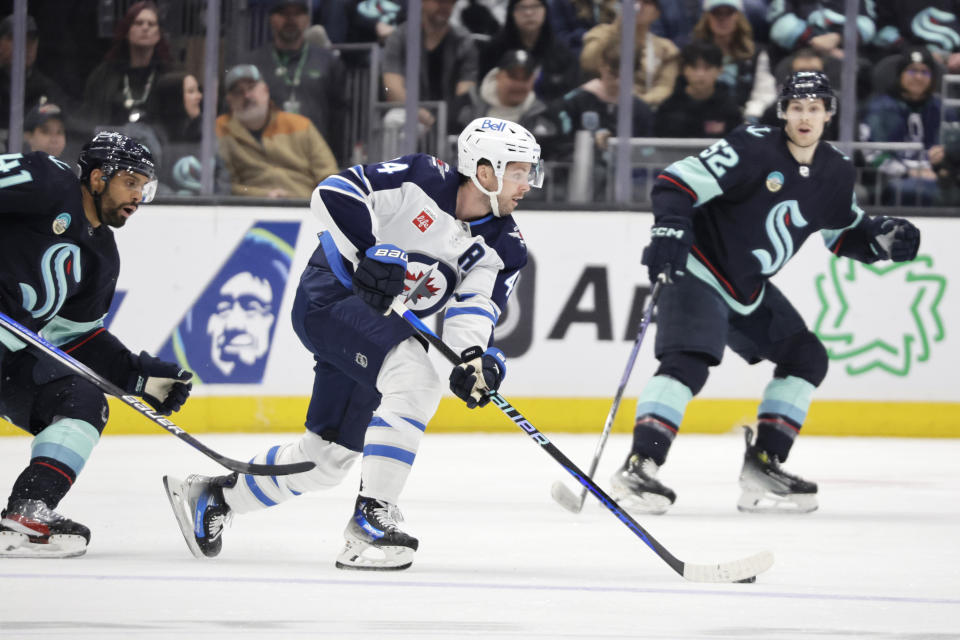 Winnipeg Jets defenseman Josh Morrissey (44) skates with the puck as Seattle Kraken left wing Pierre-Edouard Bellemare (41) and left wing Tye Kartye (52) defend during the first period of an NHL hockey game, Friday, March 8, 2024, in Seattle. (AP Photo/John Froschauer)