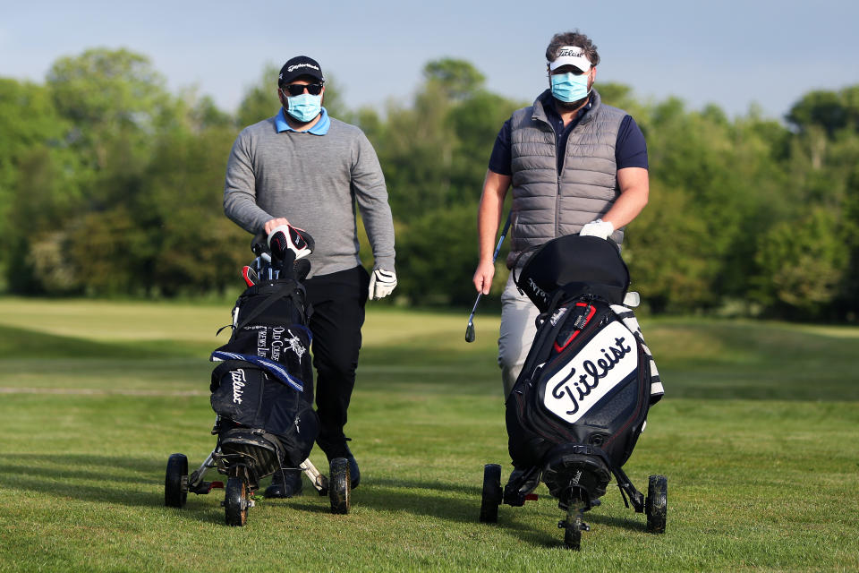 Golfers, wearing protective masks, push their trollies at Rookwood Golf Club, Horsham, Sussex, after golfers return to play as restrictions are lifted in England, as the UK continues in lockdown to curb the spread of coronavirus during the pandemic.