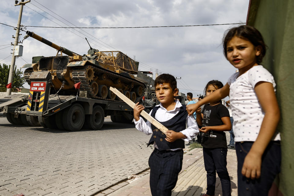 Children watch as army tanks are transported on trucks in the outskirts of the town of Akcakale, in Sanliurfa province, southeastern Turkey, at he border of Syria, Thursday, Oct. 17, 2019. U.S. Vice President Mike Pence, heading a delegation that includes Secretary of State Mike Pompeo and White House national security adviser Robert O'Brien, arrived in Turkey on Thursday, a day after Trump dismissed the very crisis he sent his aides on an emergency mission to douse.(AP Photo/Emrah Gurel)