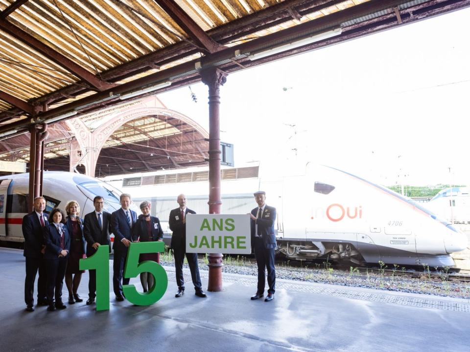 People gathered at a terminal celebrating the partnership between DB and SNCF. The row pf people are holding a banner and a cutout of the number 15.
