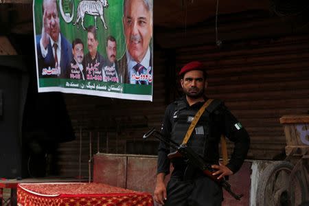 A police officer stands guard next to an electoral poster during a campaign rally ahead of general elections in the Lyari neighborhood in Karachi, Pakistan June 26, 2018. Picture taken June 26, 2018. REUTERS/Akhtar Soomro