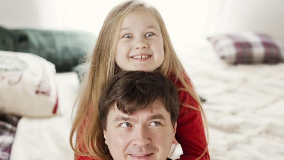 smiling father with daughter sitting on bed and having fun at home