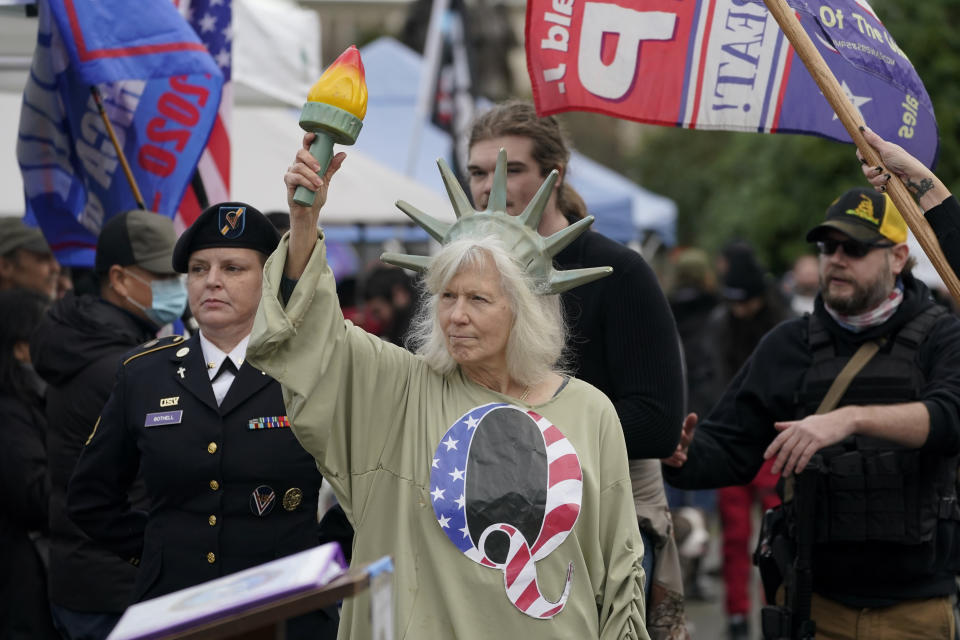 En esta imagen del 6 de enero de 2021, una persona vestida como la "Dama de la Libertad" porta una camiseta con la letra Q, en referencia a QAnon, mientras manifestantes realizan una protesta en el Capitolio de Olympia, Washington, en contra del conteo de votos electorales en Washington DC, para ratificar la victoria del presidente electo, Joe Biden. (AP Foto/Ted S. Warren, Archivo)