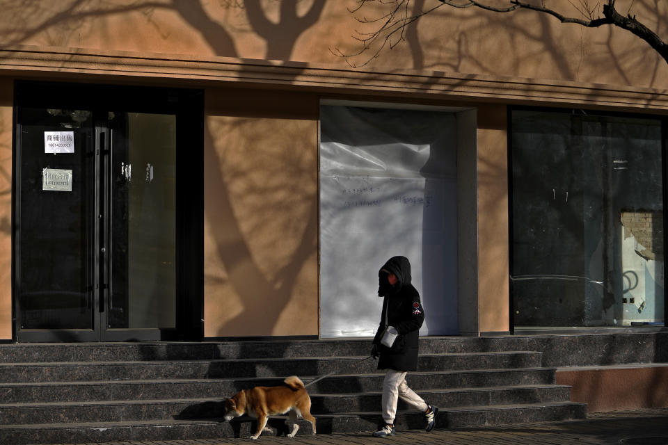 A woman wearing a face mask walks a dog passing by shuttered business shops for rent in Beijing, Tuesday, Jan. 17, 2023. China’s economic growth fell to 3% last year under pressure from antivirus controls and a real estate slump but is gradually reviving after restrictions that kept millions of people at home were lifted. (AP Photo/Andy Wong)