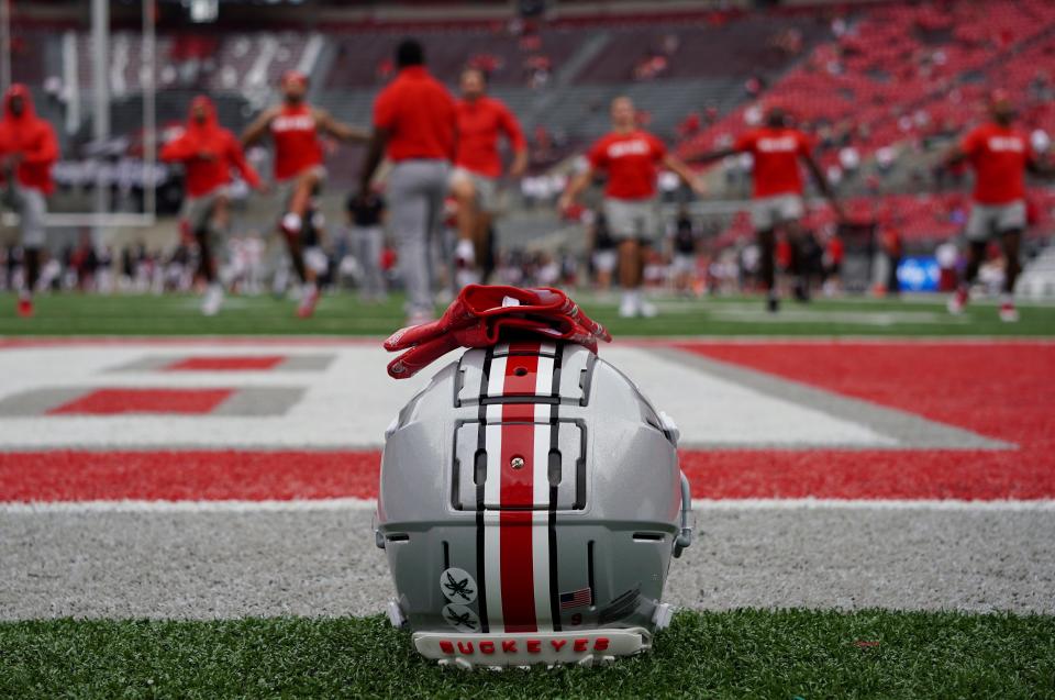 An Ohio State football helmet next to the field at Ohio State while Buckeyes football players warm up.