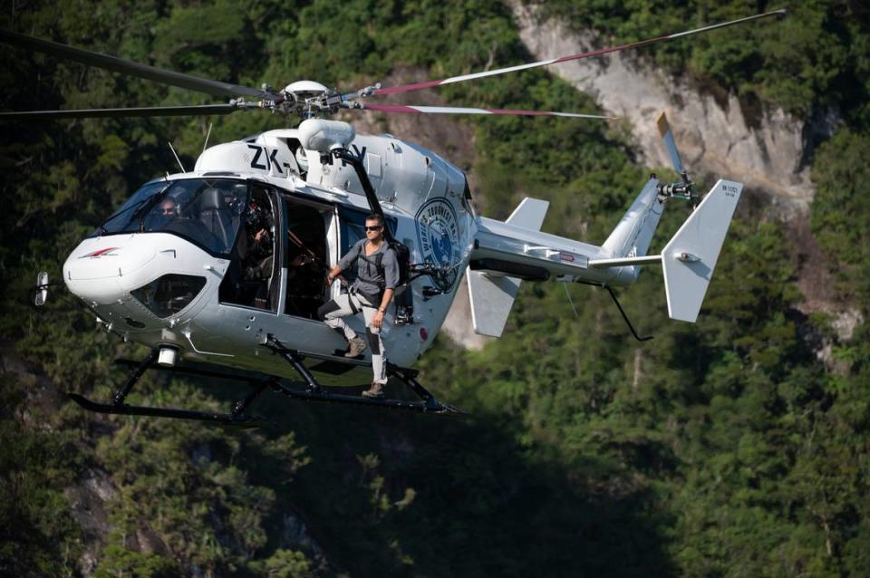 Bear Grylls rides on the side of a helicopter during the 2019 Eco-Challenge adventure race in Fiji on Monday, Sept. 9, 2019. “World’s Toughest Race: Eco-Challenge Fiji premieres on Amazon Prime on Friday, Aug. 14, 2020. 