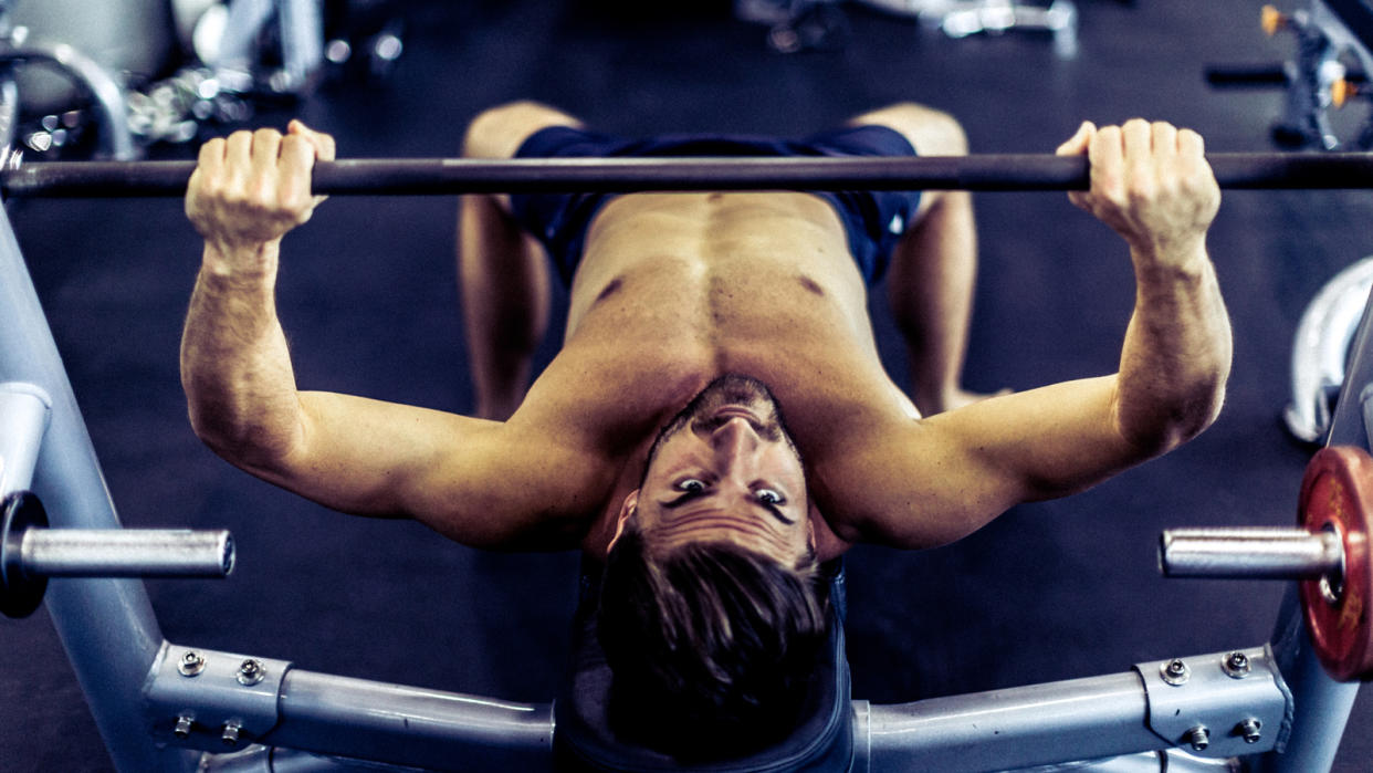  Shirtless men performing bench press in gym. 