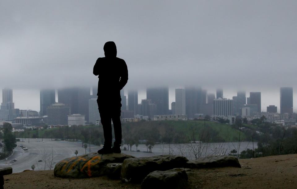 A person watches rain clouds shrouding the skyline of downtown Los Angeles.