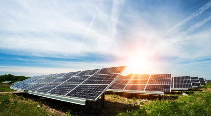 Solar panels in an open area, with the sun shining over them; solar stocks