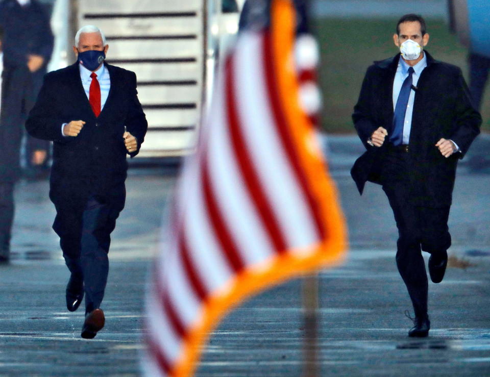 Vice President Mike Pence, with a plane gangway behind him, runs from a plane, with a Secret Service agent beside him.