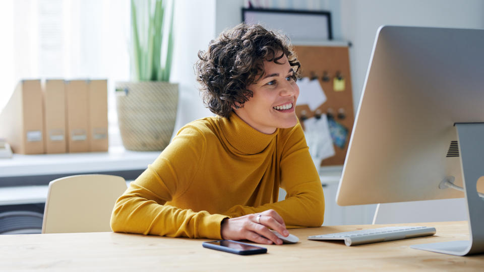 Cheerful beautiful graphic designer working on project while using computer in modern office.