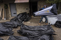 A man carries a coffin next to plastic bags with corpses of civilians as police conduct investigations in Bucha, before sending the copses to the morgue, on the outskirts of Kyiv, Ukraine, Wednesday, April 6, 2022. (AP Photo/Rodrigo Abd)