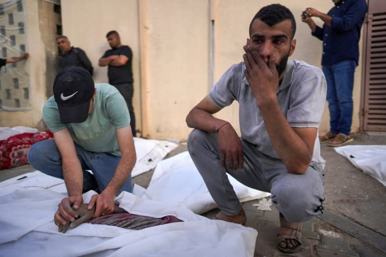 In the yard of Al-Aqsa Martyrs Hospital in Deir al-Balah, central Gaza, a Palestinian man reacts as another holds the hand of a person killed in Israeli bombardment (-)