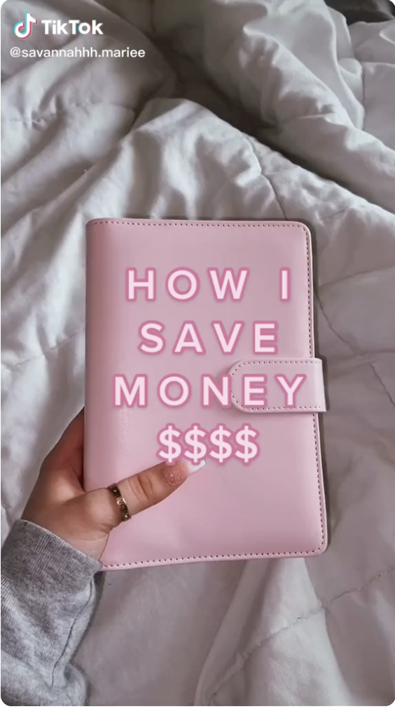 A hand holding a pink binder with text on the screen that reads, "How I save money $$$$"