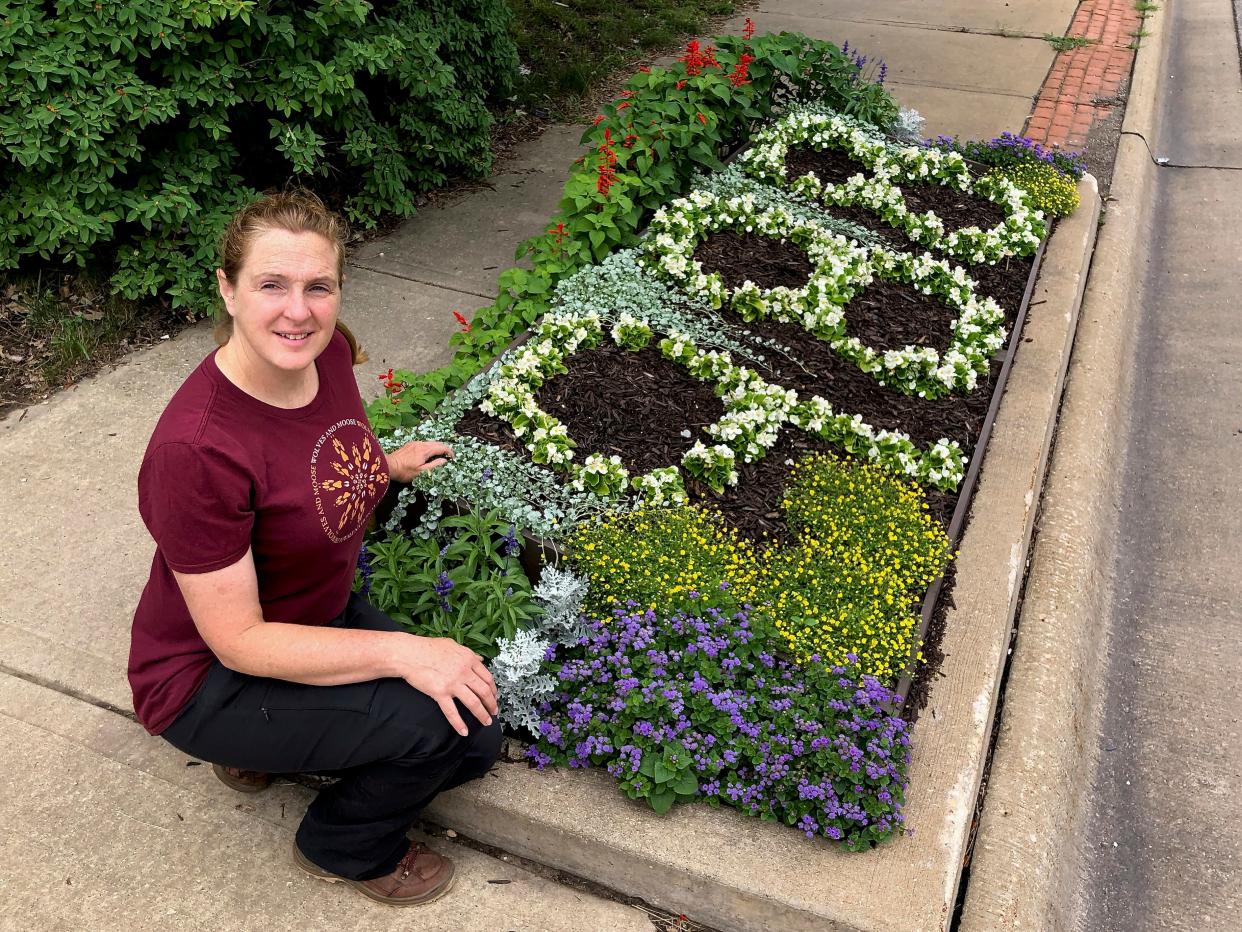 Megan Pease of Rockford, seen here on Saturday, July 16, 2022, kneels next to the flower bed she designed and planted spelling out the new suicide & crisis hotline number 988 on Auburn Street near Cumberland Street in Rockford.