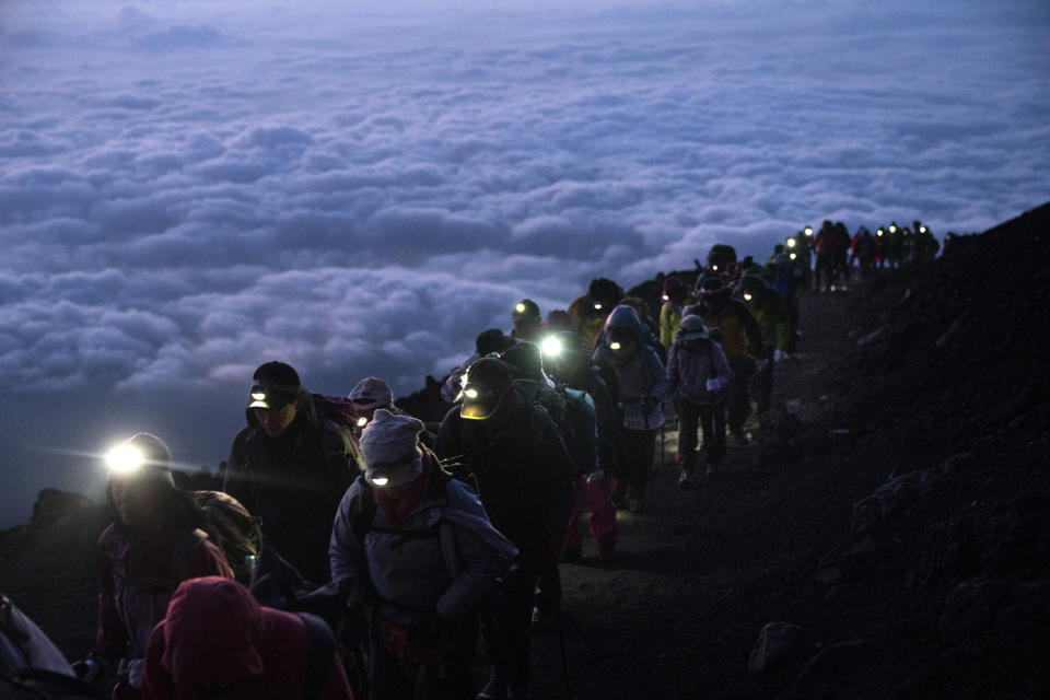 FILE -A group of hikers climb to the top of Mount Fuji just before sunrise as clouds hang below the summit Tuesday, Aug. 27, 2019, in Japan. Those who want to climb one of the most popular trails of the iconic Japanese Mount Fuji will now have to reserve ahead and pay a fee as the picturesque stratovolcano struggles with overtourism, littering and those who attempt rushed “bullet climbing,” putting lives at risk.(AP Photo/Jae C. Hong, File)