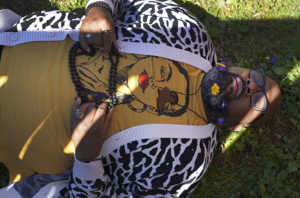 Lama Rod Owens lies in the yard of his childhood home while he poses for a portrait in Rome, Georgia,on Saturday, March 30, 2024. Owens, a self-proclaimed Black Buddhist Southern Queen, grew up Christian and was raised by his Methodist minister mother. Today, he is an influential voice in a new generation of Buddhist teachers, respected for his work focused on social change, identity and spiritual wellness. (AP Photo/Jessie Wardarski)